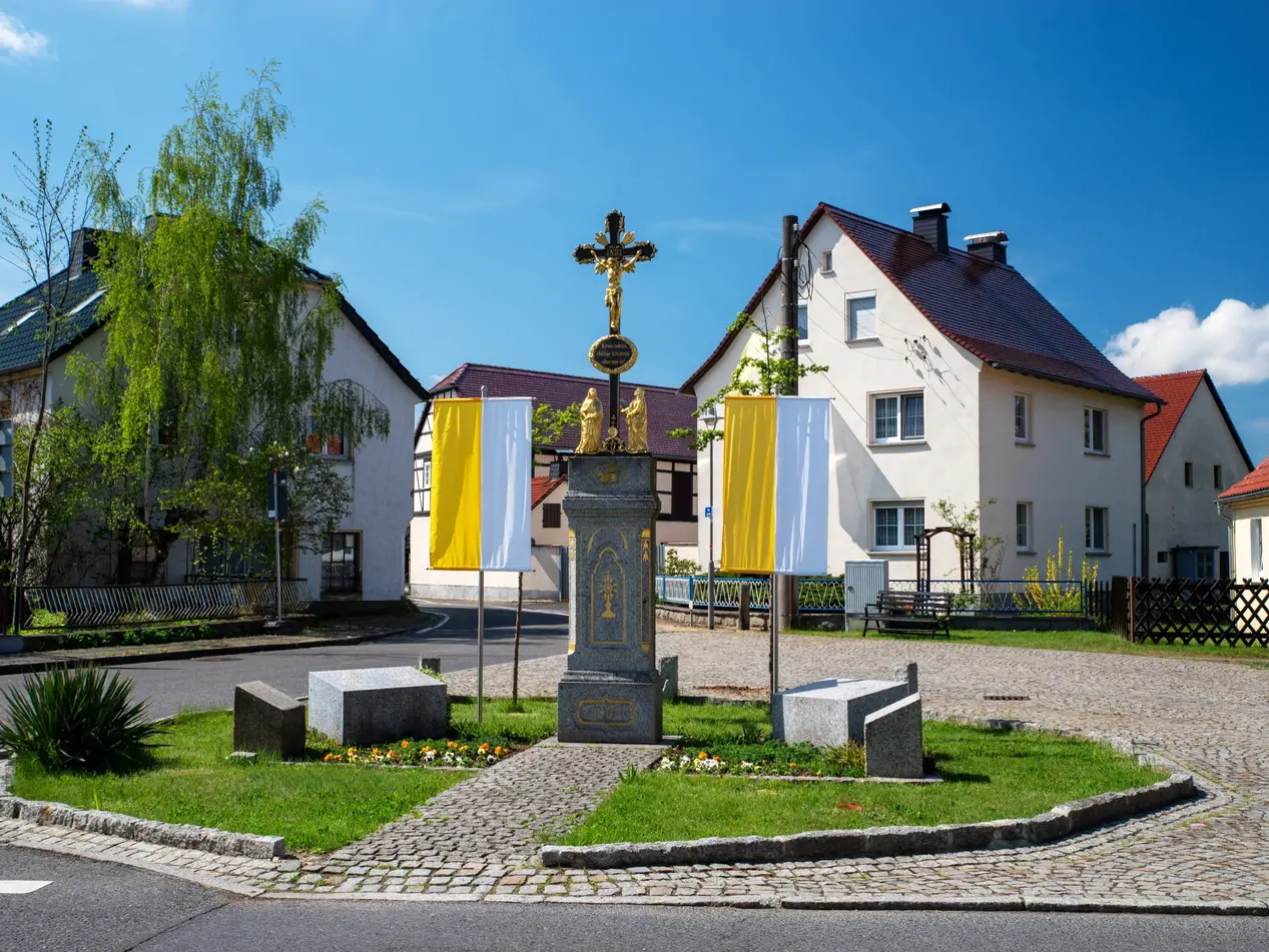 Sorbisches Dorf mit Osterschmuck - © tanja_riedel, adobe stock Geschmücktes Wegkreuz in einem sorbischen Dorf der Lausitz, mit gelb-weißen Kirchenfahnen zur Osterzeit
