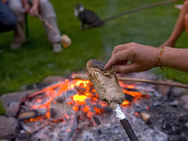 Knisterndes Feuer und glühende Kohlen – Stockbrot wird über der Glut zubereitet, ein gemütlicher Moment am Lagerfeuer. 