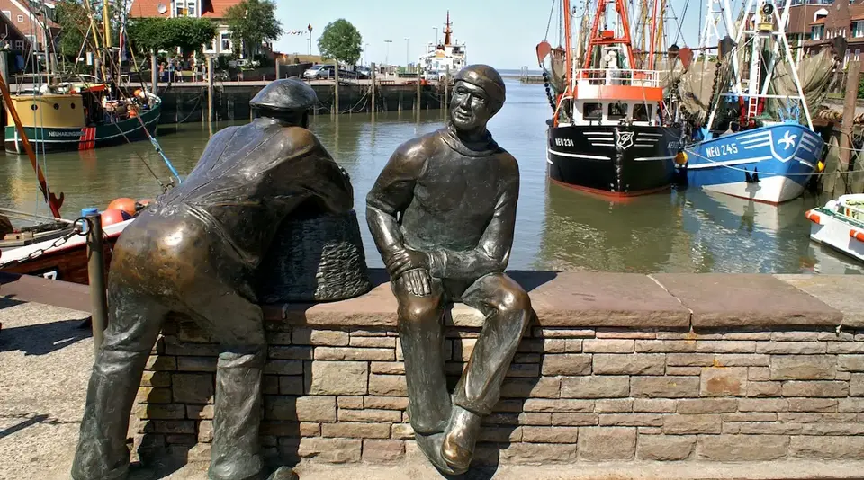 Zwei Fischer-Skulpturen blicken auf ein Hafenbecken 