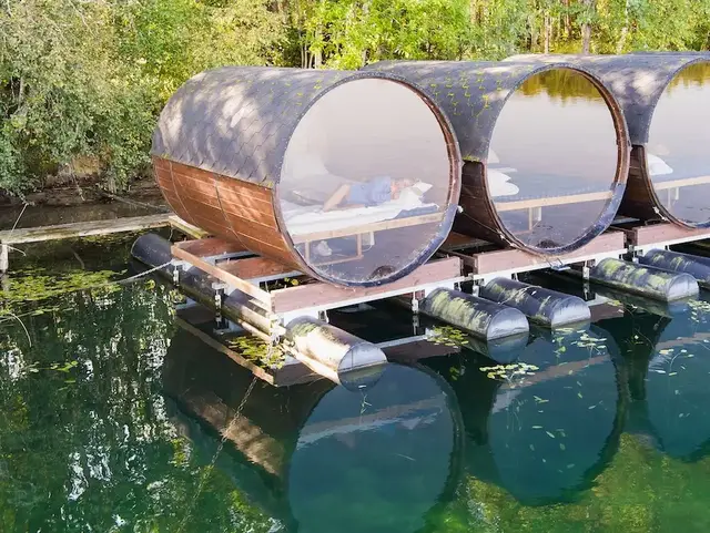 Mehrere Holz-Weinfässer als Unterkünfte am Seeufer mit Spiegelung im Wasser