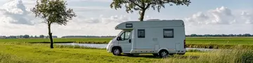 Ein weißer Campervan steht inmitten einer lebendigen Landschaft, eingerahmt von zwei Bäumen unter einem Himmel mit flauschigen Wolken – das Bild strahlt ein Gefühl von Freiheit aus.