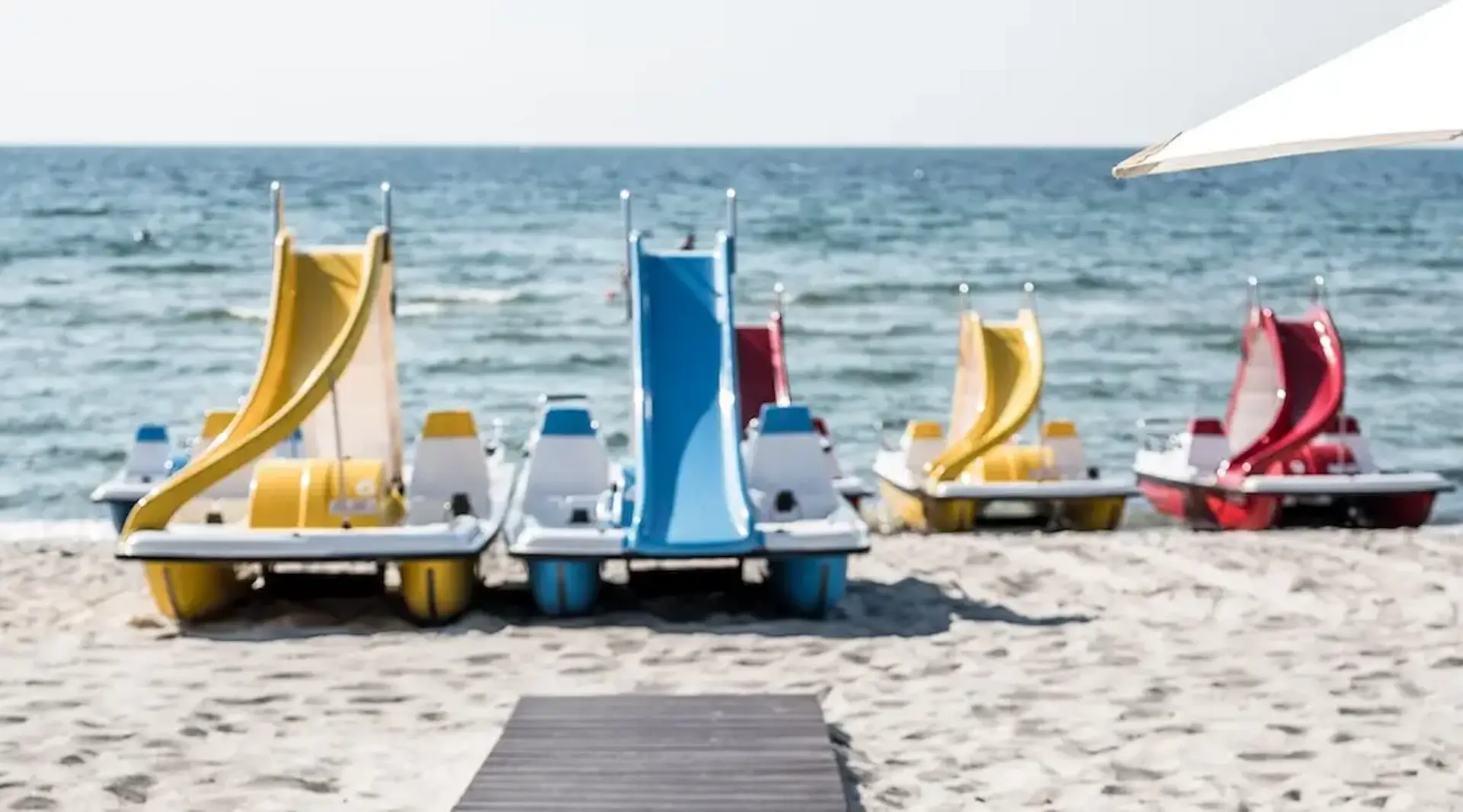 Bunte Tretboote liegen startbereit am Südstrand der Insel Fehmarn vor der Kulisse der Ostsee. 
