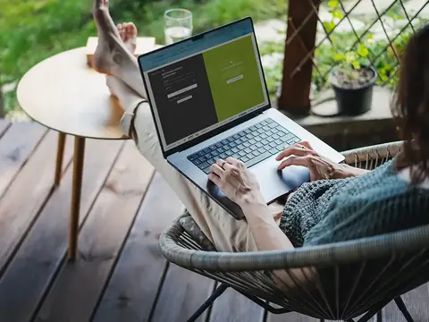 alt="Frau sitzt mit Laptopf auf dem Schoß in einem Netzstuhl auf der Terasse und logt sich bei Dreamway-Travel ein."