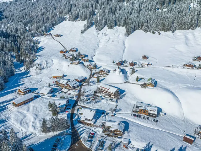 Verschneites Bergdorf Baad im hinteren Kleinwalsertal in Vorarlberg mit traditionellen Häusern und schneebedeckten Bergen.