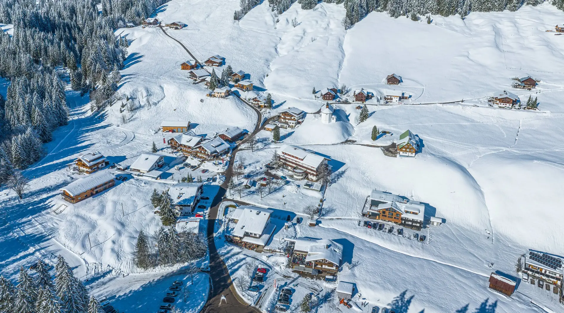 Verschneites Bergdorf Baad im hinteren Kleinwalsertal in Vorarlberg mit traditionellen Häusern und schneebedeckten Bergen.