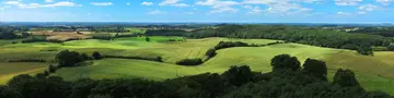 Eine hügelige grüne Landschaft mit Feldern, Wäldern und weitem Horizont in der Holsteinischen Schweiz steht für einen Bauernhof Urlaub auf dem Land.