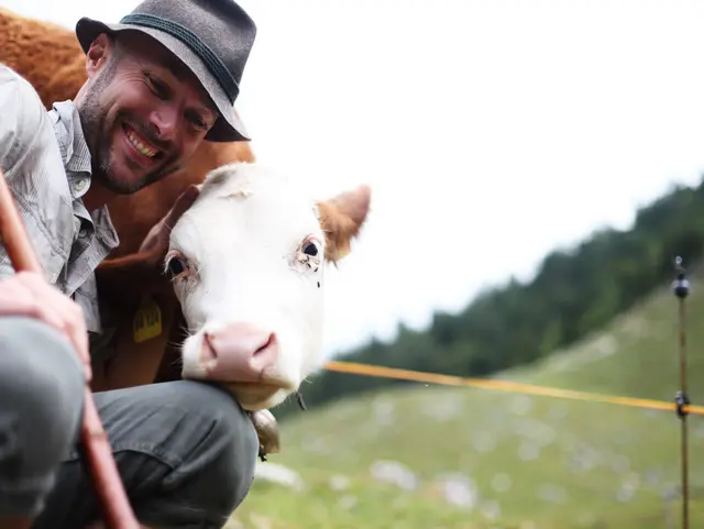 Hirte mit Kühen auf einer Weide in alpiner Landschaft als Motiv für Landurlaub in den Bergen.
