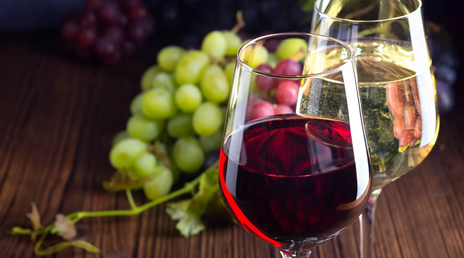 Glasses with red and white wine with grapes on wooden background