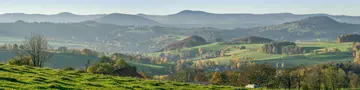 Panoramablick über die grünen Hügel, Wiesen und bewaldeten Höhenzüge der Rhön in Hessen.