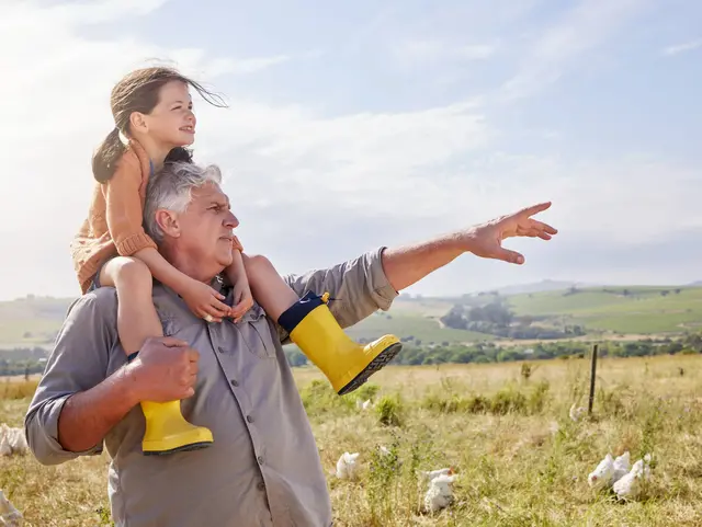 Girl, grandfather and teaching at farm, outdoor and smile on shoulders, point and organic poultry production in summer. Senior man, kid and care in nature, love or learning with chicken in Australia