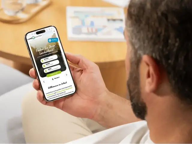 Mit Landsichten.de einfach Urlaub auf dem Land buchen Mann sitzt am Tisch und sieht sich auf dem Smart-Phone die Landsichten Startseite an.