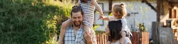 Happy young family enjoy spending time together on weekend at the countryside. Mother, father and two kids walking near their wooden country house. Moving from urban areas to rural areas concept