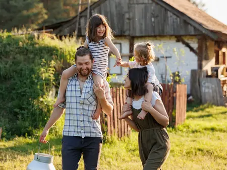 Happy young family enjoy spending time together on weekend at the countryside. Mother, father and two kids walking near their wooden country house. Moving from urban areas to rural areas concept