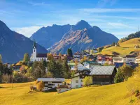 Blick auf Hirschegg im Kleinwalsertal in Vorarlberg mit umliegenden Bergen und herbstlich gefärbter Landschaft.