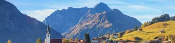 Blick auf Hirschegg im Kleinwalsertal in Vorarlberg mit umliegenden Bergen und herbstlich gefärbter Landschaft.