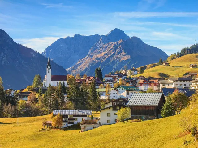Blick auf Hirschegg im Kleinwalsertal in Vorarlberg mit umliegenden Bergen und herbstlich gefärbter Landschaft.