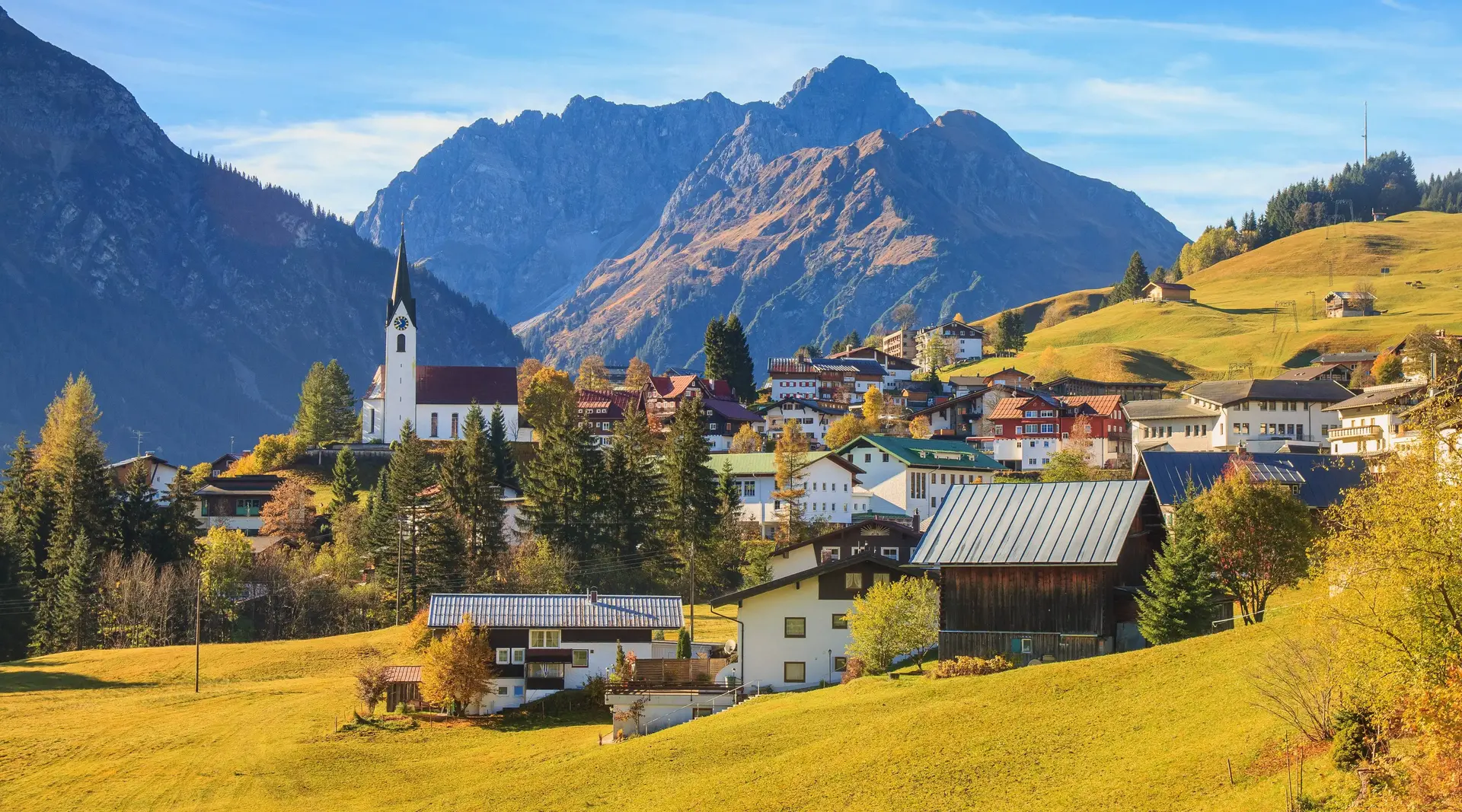 Blick auf Hirschegg im Kleinwalsertal in Vorarlberg mit umliegenden Bergen und herbstlich gefärbter Landschaft.