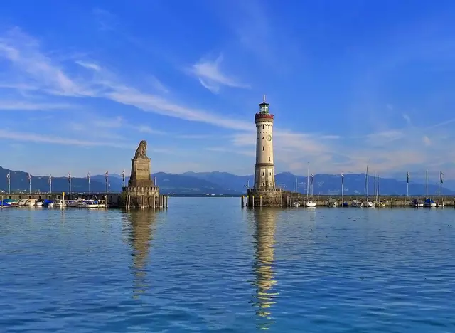 Die Stadt Lindau liegt im bayerischen Teil vom Bodensee. An der Hafeneinfahrt stehen die Statue des Bayerischen Löwen und der steinerne Lindauer Leuchtturm mit Blick auf den See und die Berge.