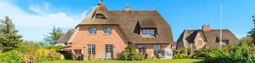 Traditionelles Ferienhaus mit Reetdach steht inmitten einer naturbelassenen Landschaft bei Kampen auf Sylt, umgeben von Wiesen, Dünen und typisch norddeutscher Architektur. 