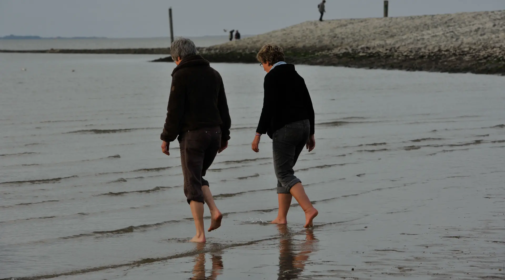 Barfuß laufen zwei Menschen im Urlaub in seichtes Wasser an der Nordsee. 