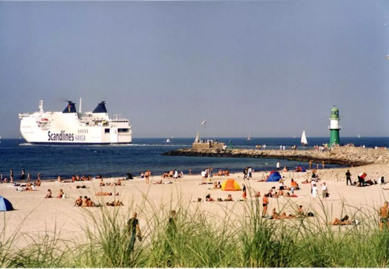 Die Fähre Scandlines legt vor Warnemünde ab und fährt vorbei am Strand und dem Leuchtturm.