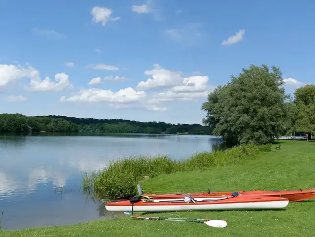 Kajakpause am See – Urlaub auf dem Land in der Holsteinischen Schweiz  - © helmut Schmidt – stock.adobe.com  Zwei rote Seekajaks liegen am Ufer eines Sees während einer Pause beim Kajakfahren in der Holsteinischen Schweiz.