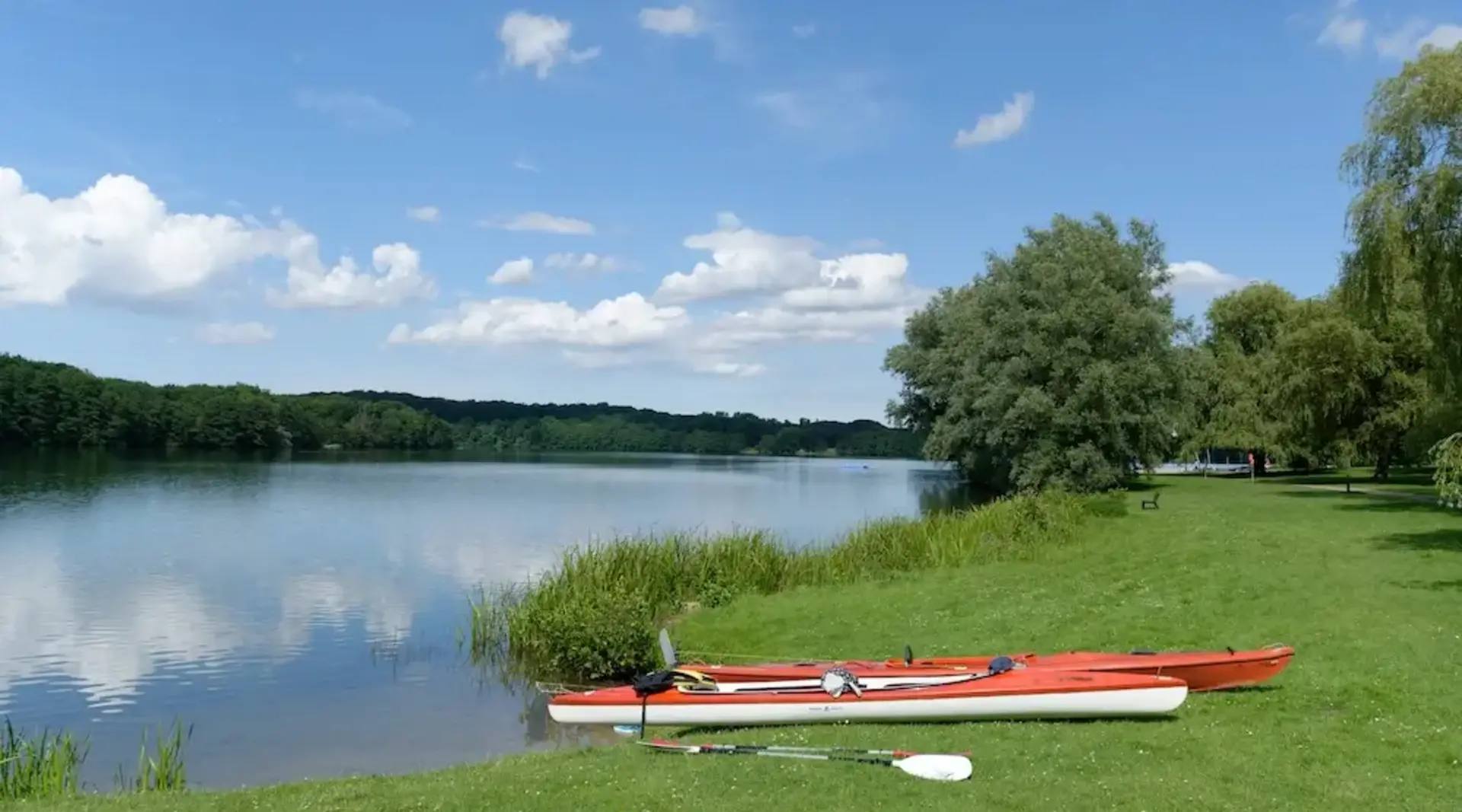 Kajakpause am See – Urlaub auf dem Land in der Holsteinischen Schweiz  - © helmut Schmidt – stock.adobe.com  Zwei rote Seekajaks liegen am Ufer eines Sees während einer Pause beim Kajakfahren in der Holsteinischen Schweiz.