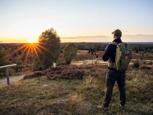 Wanderer sieht sich den Sonnenuntergang auf dem Wilseder Berg in der Lüneburger Heide an. 
