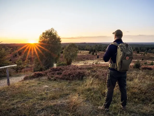 Wanderer sieht sich den Sonnenuntergang auf dem Wilseder Berg in der Lüneburger Heide an. 