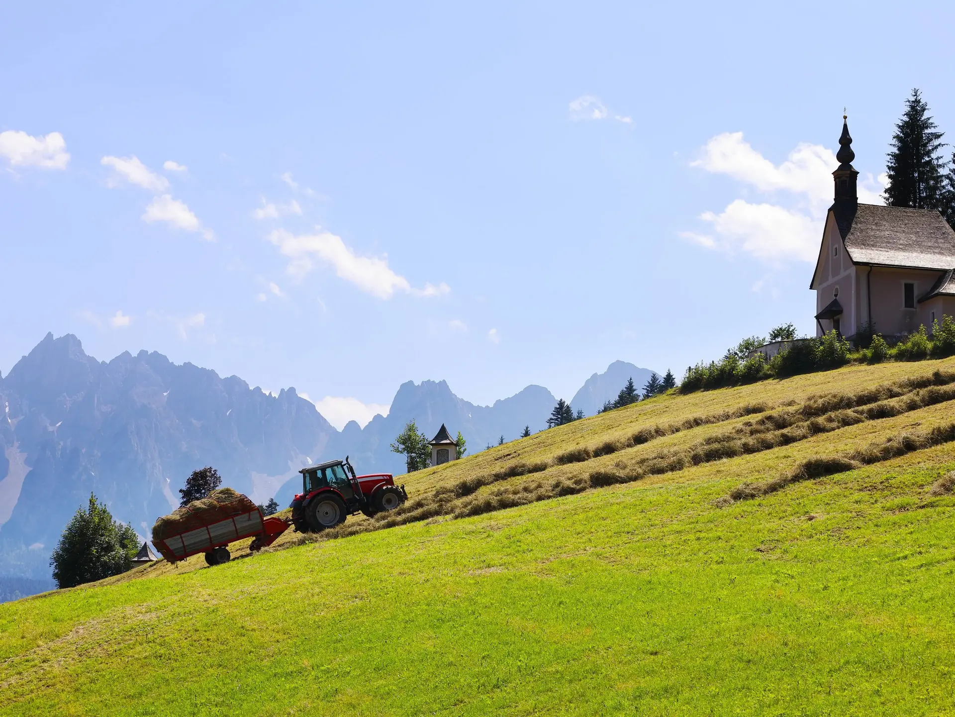 Traktor bei der Heuernte auf einer Wiese vor nebligen Bergen als Motiv für Landurlaub auf dem Bergbauernhof.
