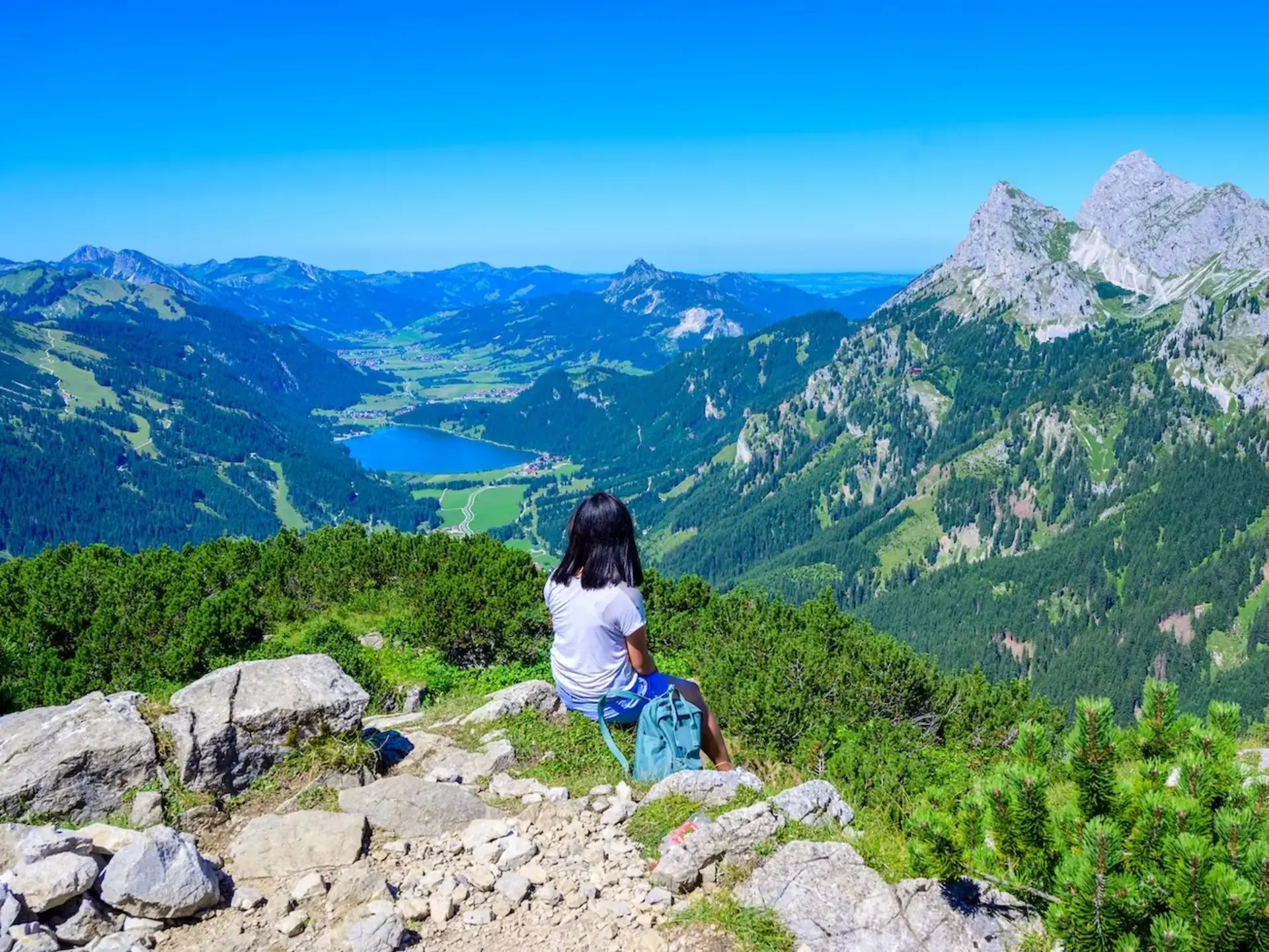 Wanderin macht eine Pause und schaut auf die Berglandschaft und einen See. 