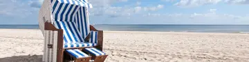 Ein weiß-blau-gestreifter Strandkorb steht am Ostseestrand und lädt zum entspannten Landurlaub in Deutschland ein. 
