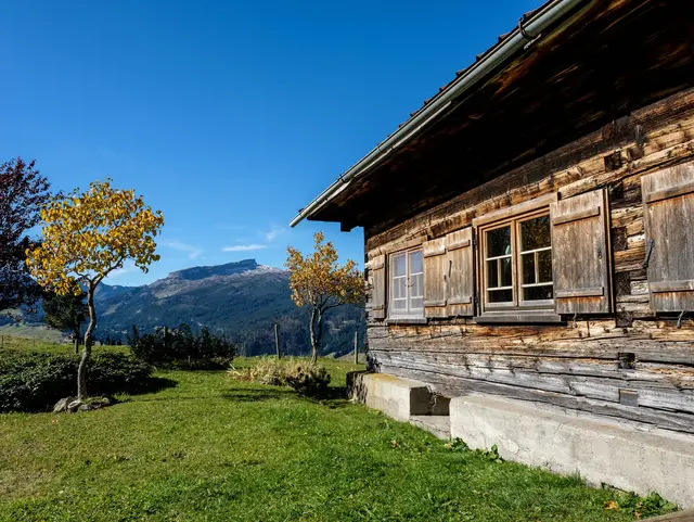 Traditionelle Holzhütte in den Bergen des Kleinwalsertals mit dem markanten Hohen Ifen im Hintergrund.