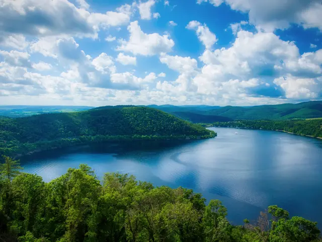Panoramablick auf den Edersee in Hessen mit tiefblauem Wasser, grünen bewaldeten Hügeln und einem Himmel mit weißen Wolken.