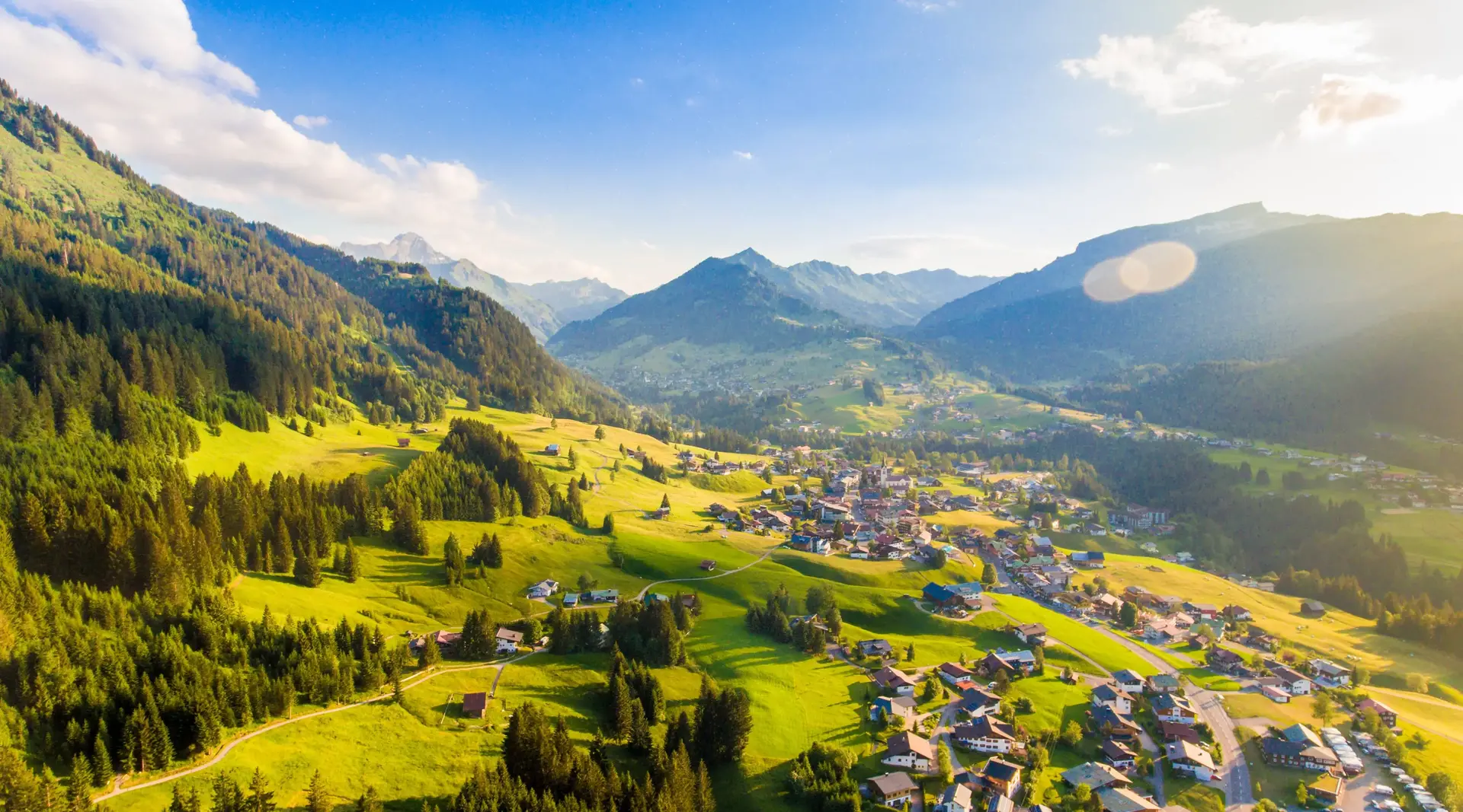 Sonniger Panoramablick auf Riezlern im Kleinwalsertal mit grünen Berghängen und umliegenden Alpengipfeln.