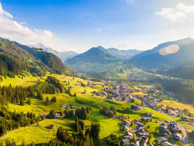 Sonniger Panoramablick auf Riezlern im Kleinwalsertal mit grünen Berghängen und umliegenden Alpengipfeln.