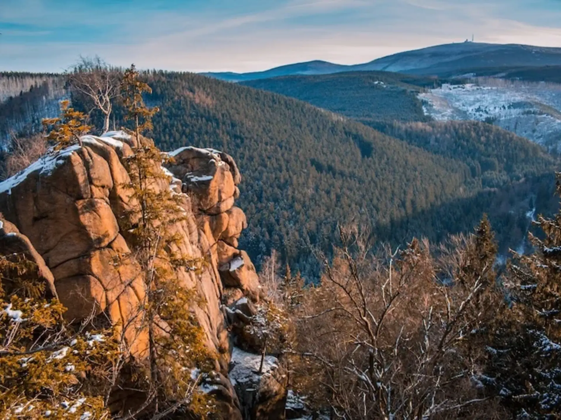 Weitläufiger Blick über sanft geschwungene, waldreiche Hügel, durchbrochen von markanten Granitfelsen, deren raue Oberflächen von Bäumen und Sträuchern umrahmt werden.