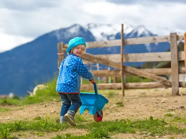 Mit anpacken auf dem Hof – Urlaub auf dem Land für Kinder - © mmphoto, adobe stock Kind schiebt eine blaue Schubkarre über einen Hofweg