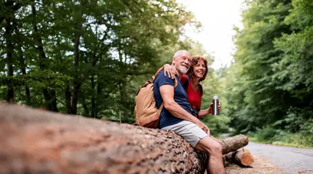 Ein fröhliches älteres Paar macht beim Wandern eine Pause im Wald 
