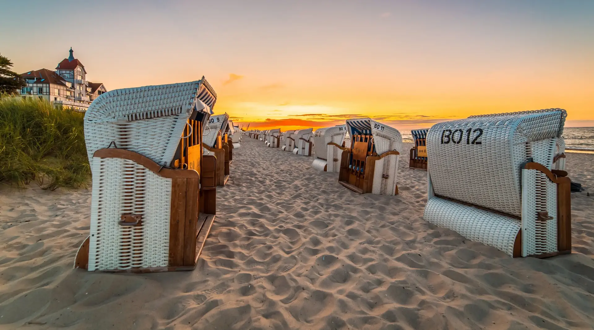 mehrere Strandkörbe stehen bei Sonnenuntergang am Sandstrand an der Ostsee, der Himmel färbt sich orange