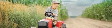 Junge mit Kindertraktor - © Jacek / AdobeStock Ein Junge fährt mit einem Kindertraktor am Feld entlang.