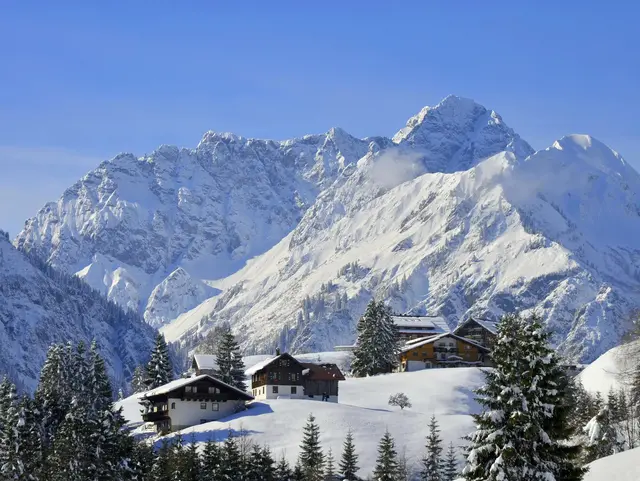 Verschneites Bergdorf im Kleinwalsertal in Österreich mit schneebedeckten Häusern und Bergen im Hintergrund.