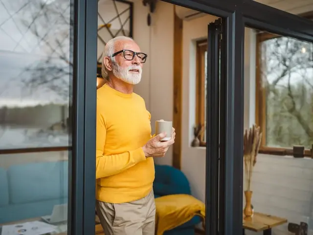 Ruhiger Moment im Tiny House – ideal für einen Urlaub auf dem Land - © Miljan Živković, adobe stock Mann steht am Fenster eines Tiny Houses in ländlicher Umgebung und blickt in die Natur