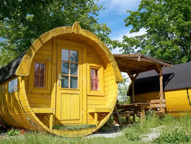 Gelbes Holz-Weinfass als Ferienunterkunft auf einer Wiese – außergewöhnliche Übernachtung im Grünen