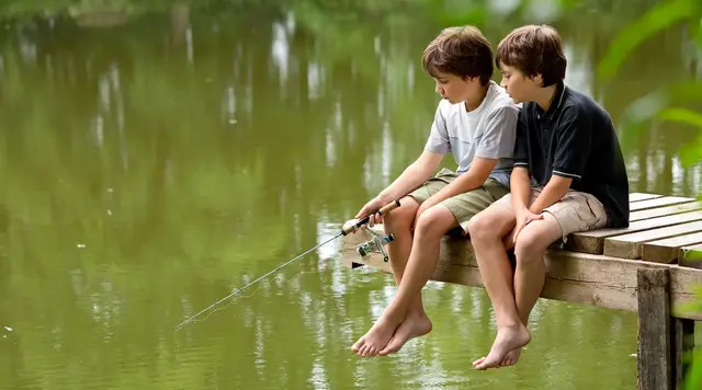 Zwei Kinder angeln an einem See von einem Holzsteg aus