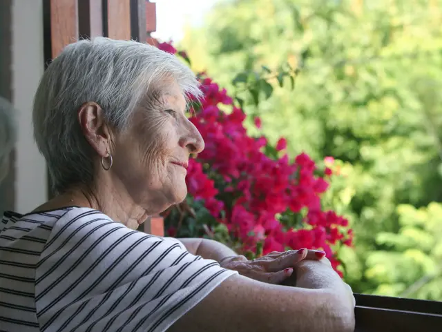 portrait of senior latino woman looking through the window at her garden