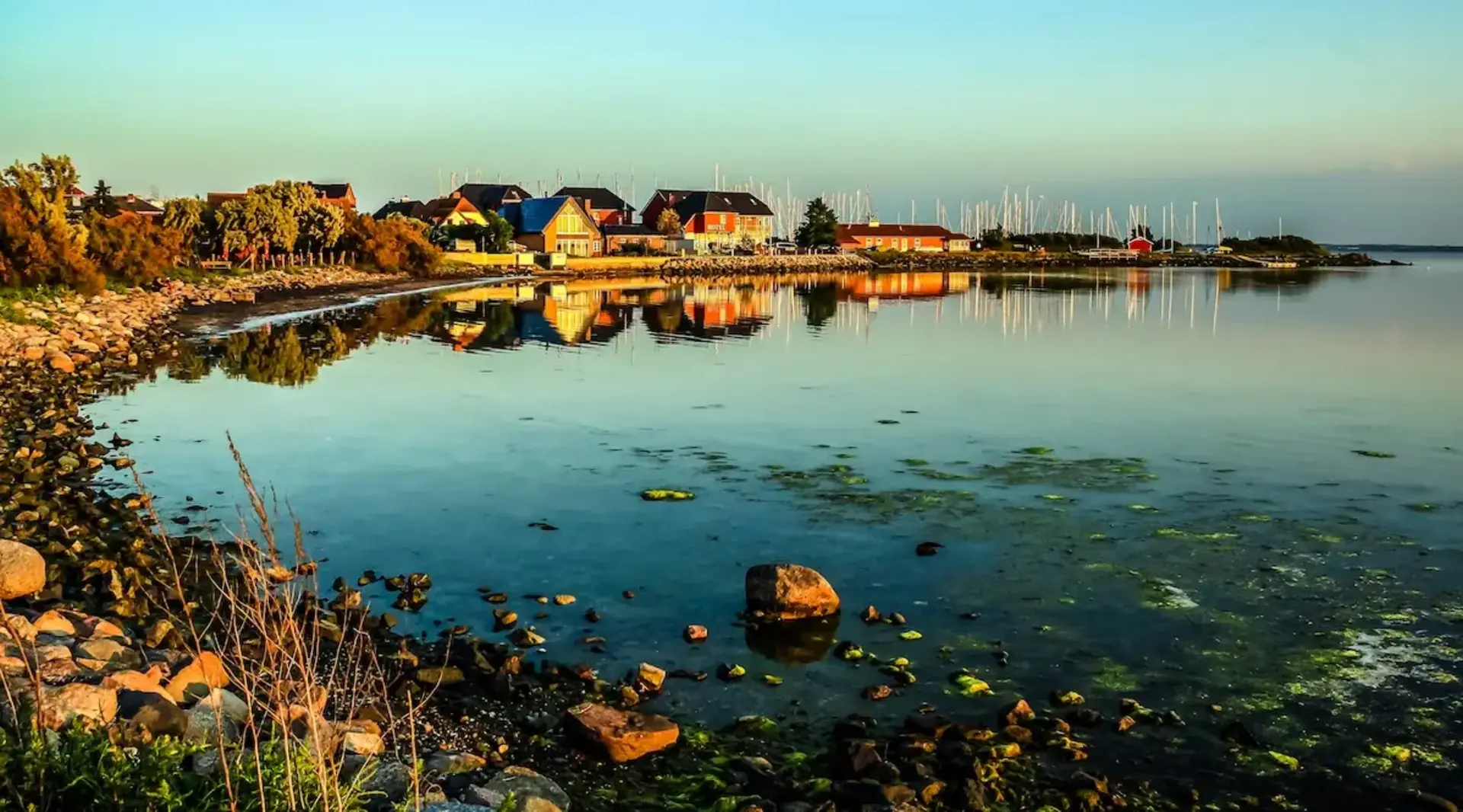 Häuser am Hafen und an der Bucht von Fehmarn sind unter einem stimmungsvollen Abendhimmel zu sehen. 