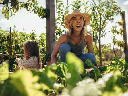 Beautiful young female farmer working in her garden with her daughter sitting by. Young mother and daughter working in the farm.