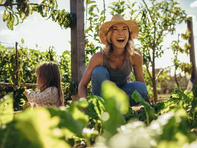 Beautiful young female farmer working in her garden with her daughter sitting by. Young mother and daughter working in the farm.