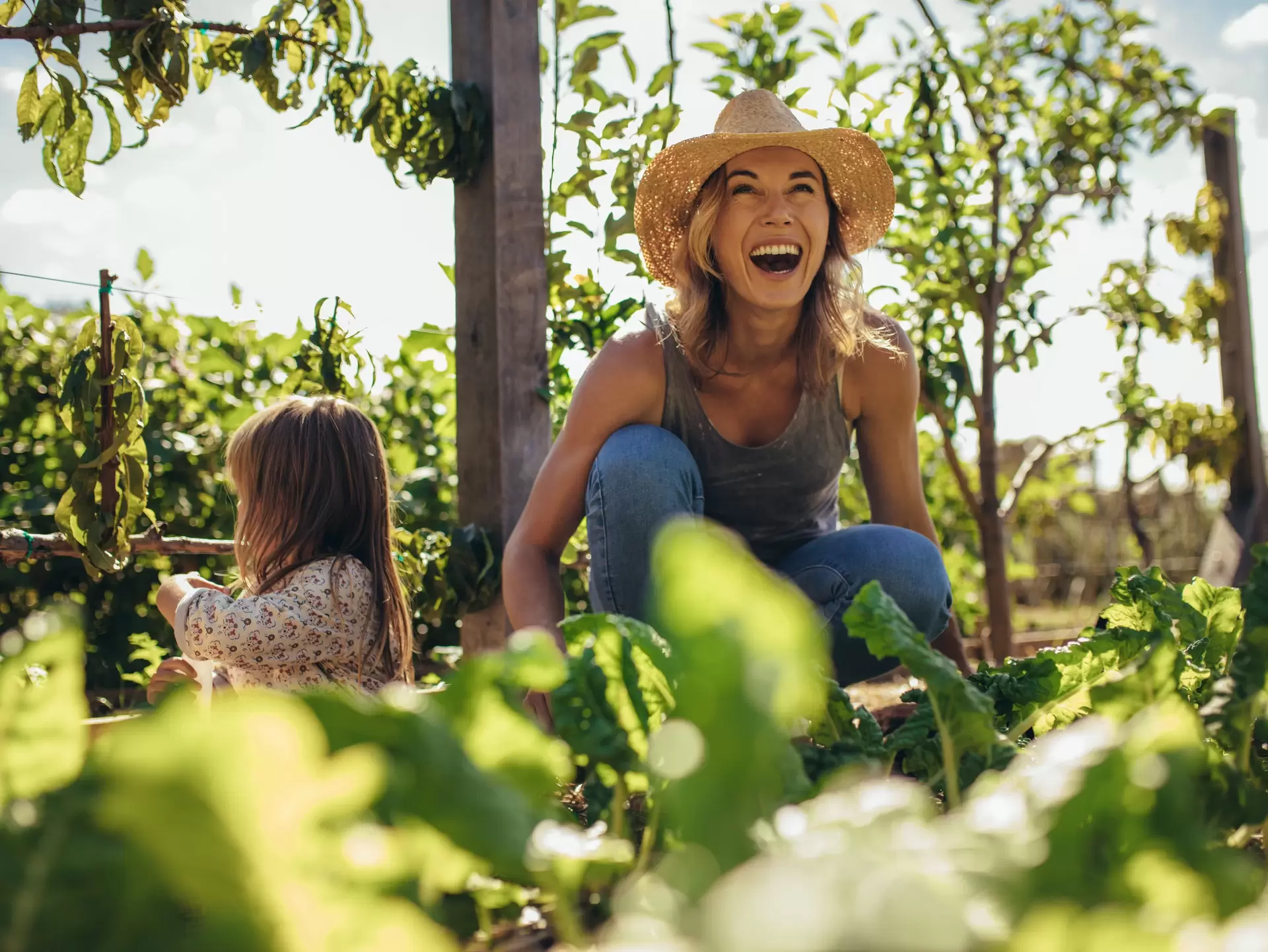 Family working on allotment together Beautiful young female farmer working in her garden with her daughter sitting by. Young mother and daughter working in the farm.